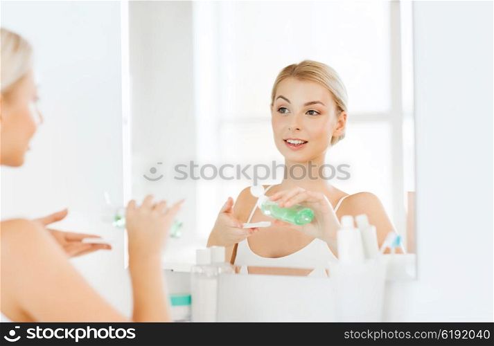 beauty, skin care and people concept - smiling young woman applying lotion to cotton disc for washing her face at bathroom