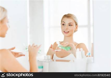 beauty, skin care and people concept - smiling young woman applying lotion to cotton disc for washing her face at bathroom