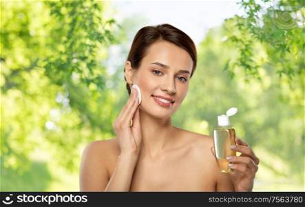beauty, skin care and people concept - smiling young woman with toner or cleanser and cotton pad cleansing face over green natural background. young woman with toner or cleanser and cotton pad