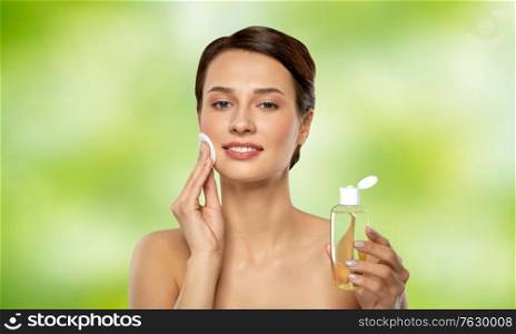 beauty, skin care and people concept - smiling young woman with toner or cleanser and cotton pad cleansing face over lime green natural background. young woman with toner or cleanser and cotton pad