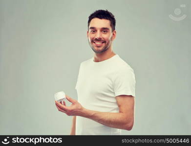 beauty, skin care, body care and people concept - smiling young man with cream jar over gray background. happy young man with cream jar over gray