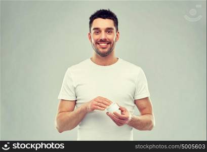 beauty, skin care, body care and people concept - smiling young man with cream jar over gray background. happy young man with cream jar over gray