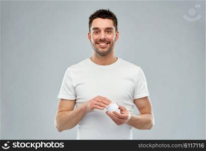 beauty, skin care, body care and people concept - smiling young man with cream jar over gray background