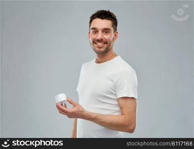 beauty, skin care, body care and people concept - smiling young man with cream jar over gray background