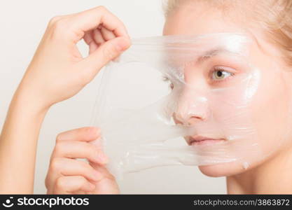 Beauty skin care cosmetics and health concept. Closeup young woman face, girl removing facial peel off mask on gray. Peeling