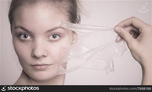 Beauty skin care cosmetics and health concept. Closeup young woman face, girl removing facial peel off mask on gray. Peeling