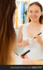 Beauty skin care cosmetics and health concept. Young woman applying facial mud clay mask to her face in bathroom