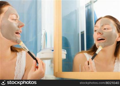 Beauty skin care cosmetics and health concept. Young woman applying facial mud clay mask to her face in bathroom
