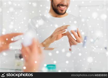 beauty, skin care, winter, christmas and people concept - close up of happy young man with facial cream at bathroom over snow