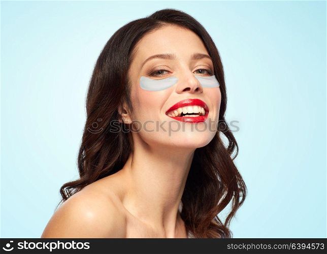 beauty, skin hydration and people concept - happy smiling young woman with hydrogel eye patches over blue background. beautiful young woman with hydrogel eye patches