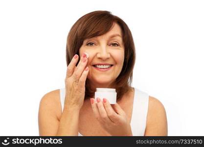 beauty, skincare and cosmetics concept - smiling senior woman applying cream to her face. smiling senior woman applying cream to her face