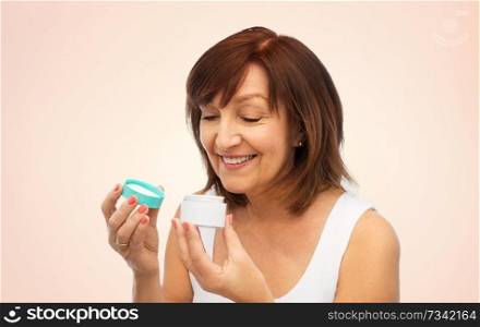 beauty, skincare and cosmetics concept - smiling senior woman with cream jar over beige background. smiling senior woman with cream jar