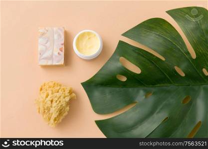 beauty, spa and bath concept - close up of crafted soap bar, natural sponge with body butter and monstera deliciosa leaf on beige background. natural soap, sponge, body butter and monstera