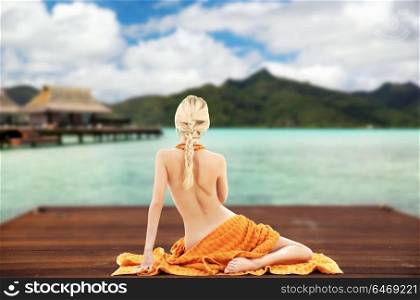 beauty, spa and travel concept - bare woman with towel on wooden pier over exotic resort and bungalow background. woman with towel over exotic resort background
