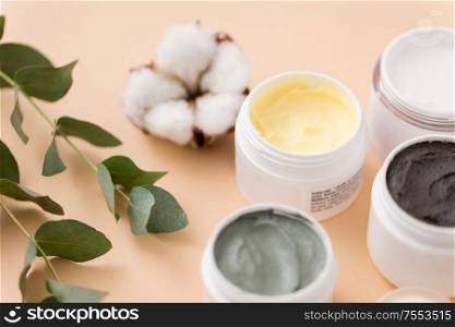 beauty, spa and wellness concept - blue clay mask, body butter, therapeutic mud and eucalyptus cinerea with cotton flower on beige background. blue clay mask, body butter and eucalyptus cinerea