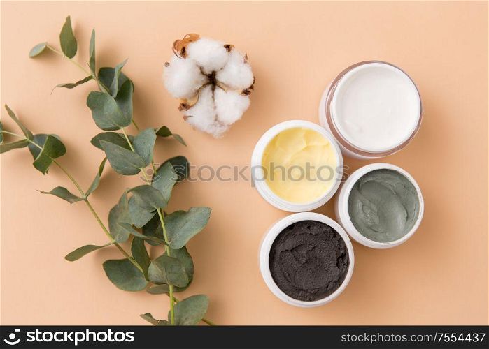 beauty, spa and wellness concept - blue clay mask, body butter, therapeutic mud and eucalyptus cinerea with cotton flower on beige background. blue clay mask, body butter and eucalyptus cinerea