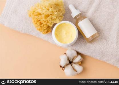 beauty, spa and wellness concept - close up of body butter, natural sponge and essential oil on bath towel. body butter, essential oil, sponge on bath towel