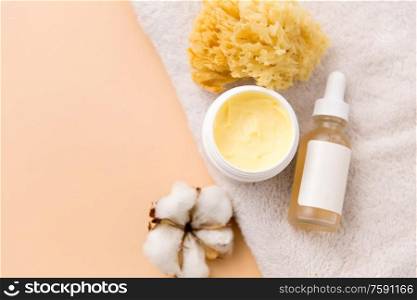 beauty, spa and wellness concept - close up of body butter, natural sponge and essential oil on bath towel. body butter, essential oil, sponge on bath towel