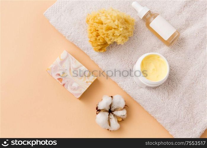 beauty, spa and wellness concept - close up of crafted soap bar, body butter, natural sponge and essential oil on bath towel. body butter, essential oil, sponge on bath towel
