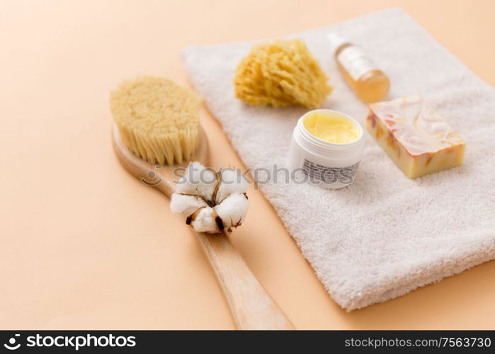 beauty, spa and wellness concept - close up of crafted soap bar, natural bristle wooden brush, body butter with sponge and essential oil on bath towel. soap, brush, sponge and body butter on bath towel