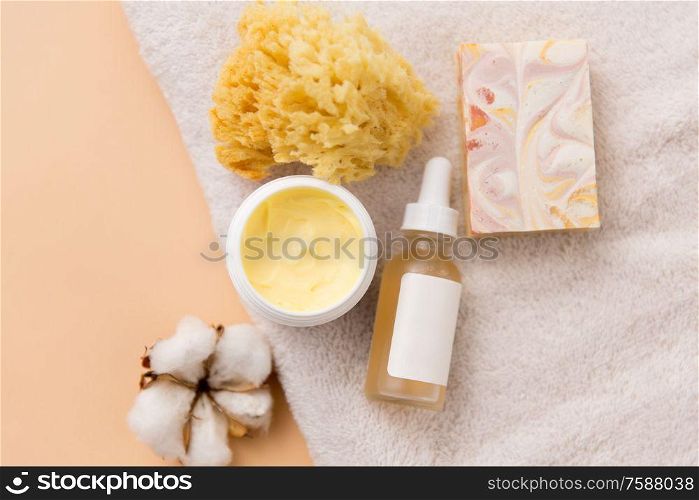 beauty, spa and wellness concept - close up of crafted soap bar, body butter, natural sponge and essential oil on bath towel. body butter, essential oil, sponge on bath towel