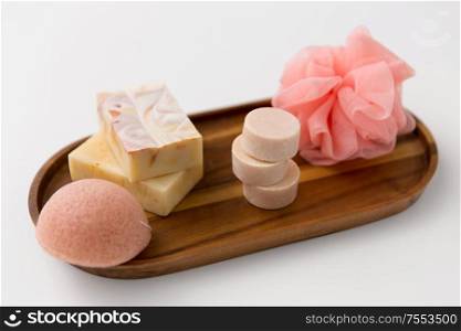 beauty, spa and wellness concept - close up of crafted soap bars, konjac sponge and wisp on wooden tray. crafted soap, sponge and wisp on wooden tray