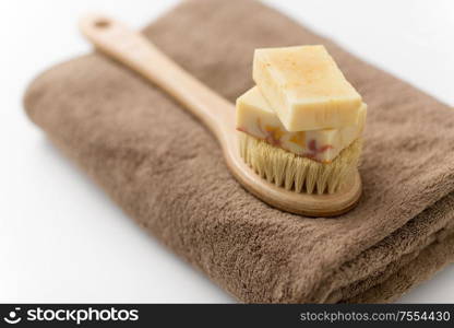 beauty, spa and wellness concept - close up of crafted soap bars and natural bristle wooden brush on bath towel. crafted soap bars, natural brush and bath towel