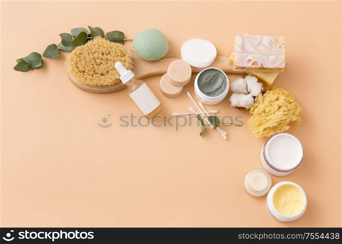 beauty, spa and wellness concept - close up of crafted soap bars, natural bristle wooden brush, body butter with sponge and serum on beige background. soap, brush, sponge, clay mask and body butter