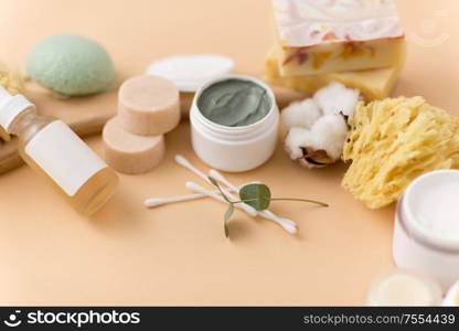 beauty, spa and wellness concept - close up of crafted soap bars, natural bristle wooden brush, body butter with sponge and herbs on beige background. soap, brush, sponge, clay mask and body butter