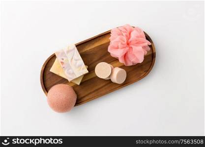 beauty, spa and wellness concept - close up of crafted soap bars, konjac sponge and wisp on wooden tray. crafted soap, sponge and wisp on wooden tray