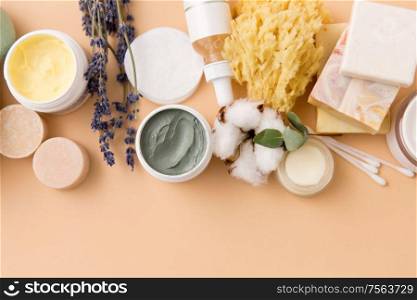 beauty, spa and wellness concept - close up of crafted soap bars, natural bristle wooden brush, body butter with sponge and herbs on beige background. soap, brush, sponge, clay mask and body butter