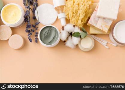 beauty, spa and wellness concept - close up of crafted soap bars, natural bristle wooden brush, body butter with sponge and herbs on beige background. soap, brush, sponge, clay mask and body butter