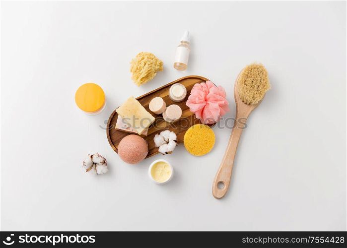 beauty, spa and wellness concept - close up of konjac sponge, crafted soap bars on wooden tray and body butter with natural bristle brush. crafted soap, sponges, brush and natural cosmetics