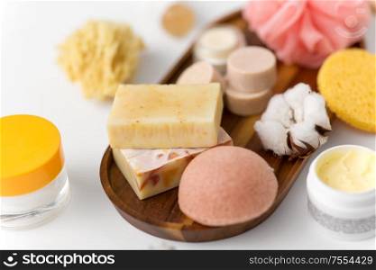 beauty, spa and wellness concept - close up of konjac sponge, crafted soap bars and body butter on wooden tray. crafted soap, sponge and wisp on wooden tray