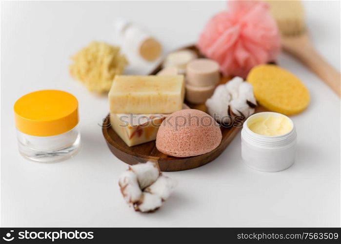 beauty, spa and wellness concept - close up of konjac sponge, crafted soap bars, body butter and cream on wooden tray. crafted soap, sponge and wisp on wooden tray