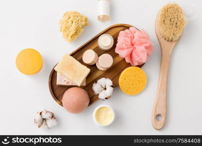 beauty, spa and wellness concept - close up of konjac sponge, crafted soap bars on wooden tray and body butter with natural bristle brush. crafted soap, sponges, brush and natural cosmetics