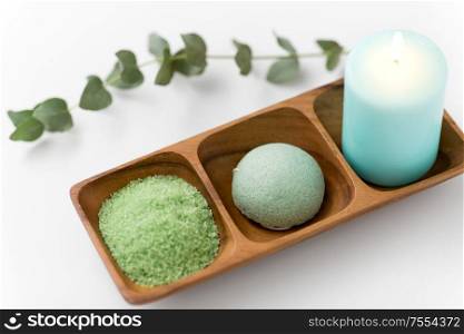 beauty, spa and wellness concept - green bath salt, konjac sponge and candle on wooden tray with eucalyptus cinerea. bath salt, konjac sponge, candle and eucalyptus