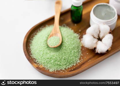 beauty, spa and wellness concept - green bath salt with wooden spoon, blue clay mask, cotton flower and serum on tray. bath salt, serum, clay mask and cotton on tray