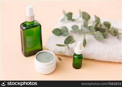 beauty, spa and wellness concept - serum, clay mask, oil and eucalyptus cinerea on bath towel. serum, clay mask, oil and eucalyptus on bath towel