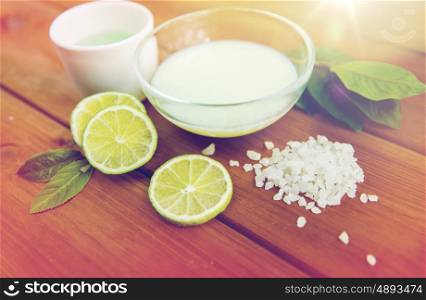 beauty, spa, body care and natural cosmetics concept - close up of bowls with citrus body lotion, cream and sea salt on wooden table