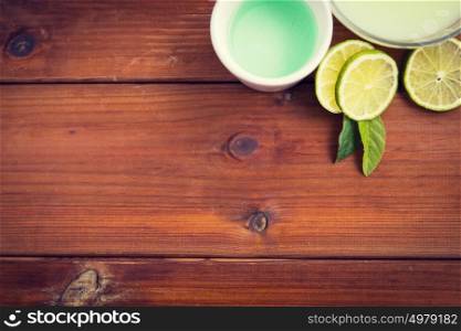 beauty, spa, body care and natural cosmetics concept - close up of bowls with citrus body lotion, cream and limes on wooden table. close up of body lotion, cream and limes on wood