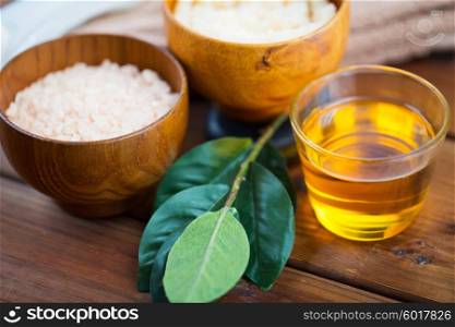 beauty, spa, body care and natural cosmetics concept - close up of honey in glass, with pink salt and leaves on wooden table