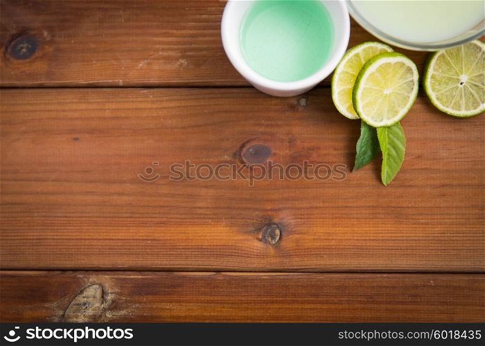 beauty, spa, body care and natural cosmetics concept - close up of bowls with citrus body lotion, cream and limes on wooden table