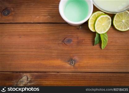 beauty, spa, body care and natural cosmetics concept - close up of bowls with citrus body lotion, cream and limes on wooden table