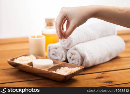 beauty, spa, body care and natural cosmetics concept - close up of hand pouring himalayan salt in wooden bowl with soap, scrub and bath towels on table