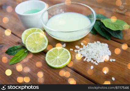 beauty, spa, body care and natural cosmetics concept - close up of bowls with citrus body lotion, cream and sea salt on wooden table