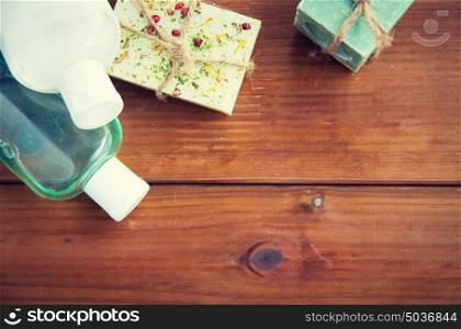 beauty, spa, body care, bath and natural cosmetics concept - close up of handmade soap bars and lotion bottles on wooden table. close up of handmade soap bars and lotions on wood