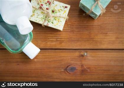 beauty, spa, body care, bath and natural cosmetics concept - close up of handmade soap bars and lotion bottles on wooden table
