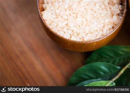 beauty, spa, body care, bath and natural cosmetics concept - close up of himalayan pink salt in wooden bowl with leaves