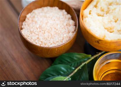 beauty, spa, body care, natural cosmetics and and wellness concept - close up of himalayan pink salt and body scrub with leaves on wooden table
